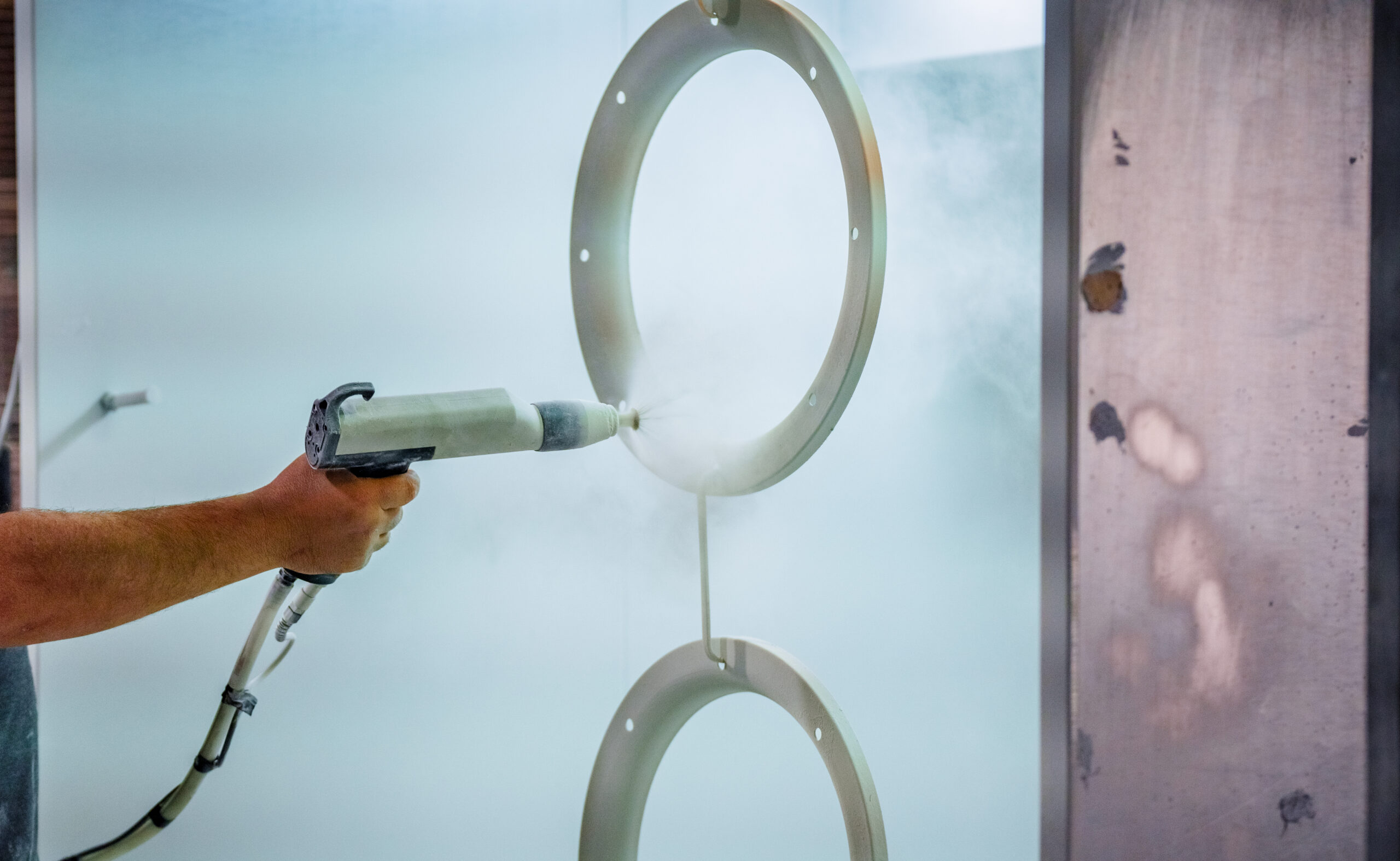 Close up of a powder coating sprayer applying a protective finish to a metal ring.